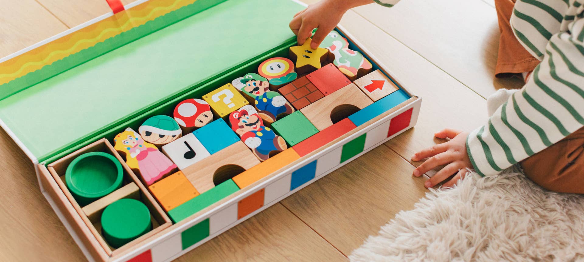 Foto promocional mostrando a un niño pequeño alcanzando un gran contenedor con bloques de madera temáticos de Mario.